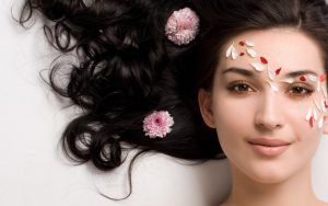 Portrait of Fresh and Beautiful brunette woman laying on grey  background around pink flowers